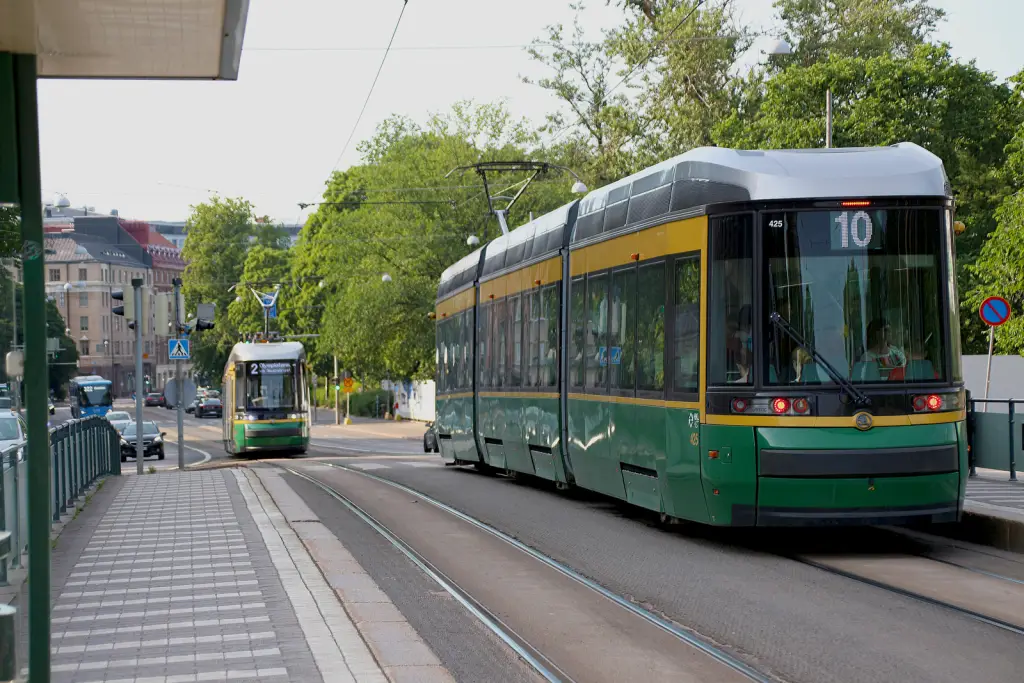 Two trams on a sunny street in Helsinki, Finland, surrounded by greenery.