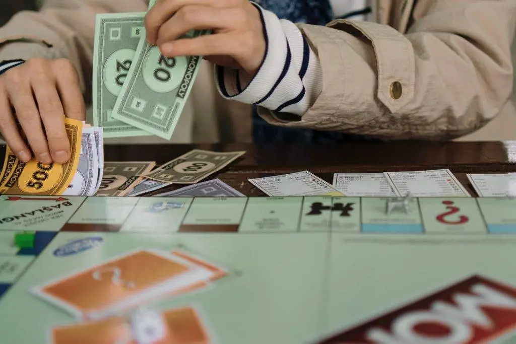Hands counting Monopoly money during a board game session, highlighting fun and strategy.