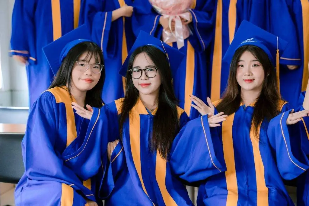 Three graduates in blue gowns celebrating their achievement indoors.