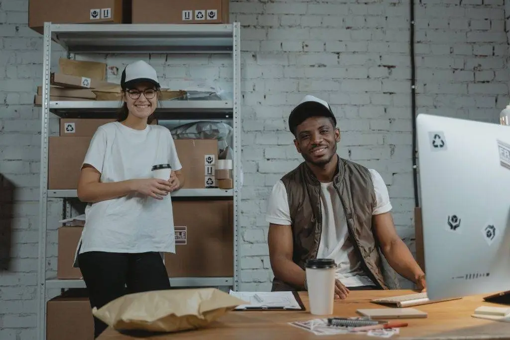 Two warehouse employees in casual attire smiling while working in a courier environment with packages.