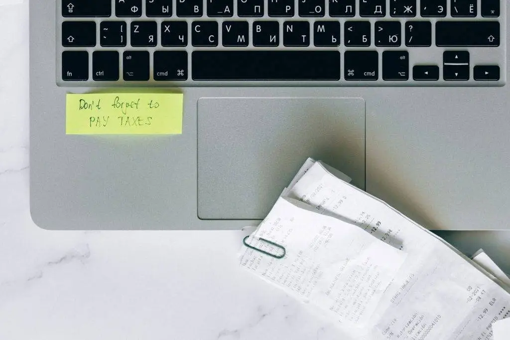 A laptop with a sticky note reminder and receipts, emphasizing tax season organization.