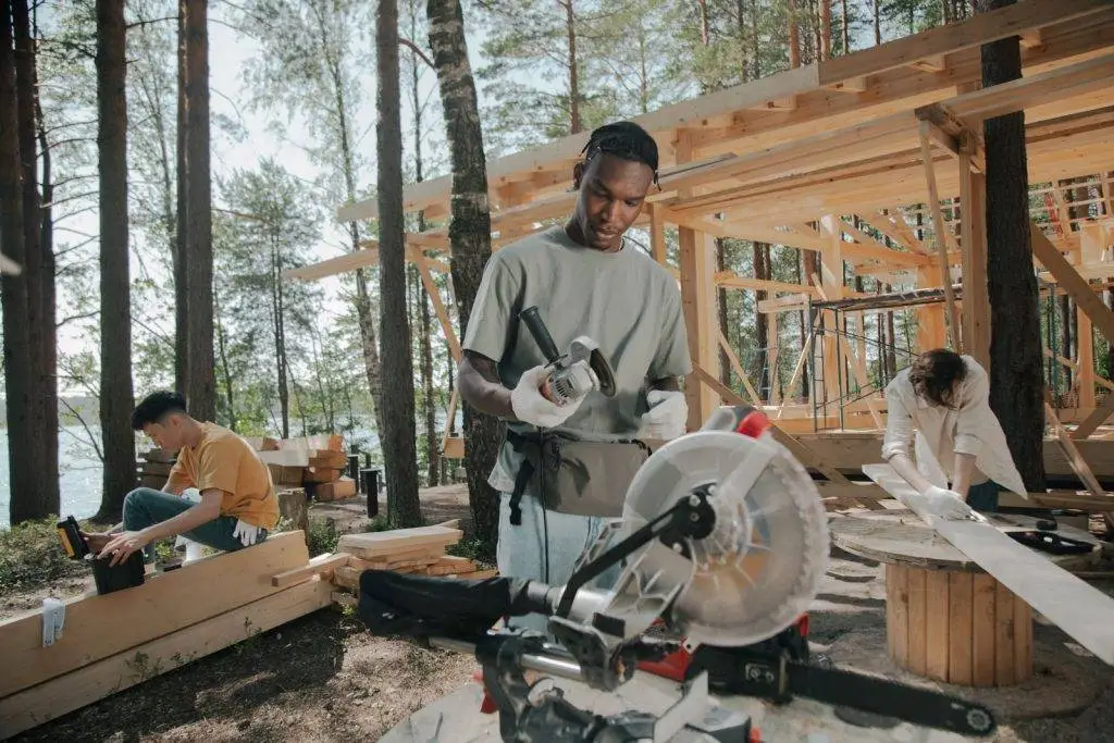 Construction crew building a wooden structure outdoors in a forest setting.